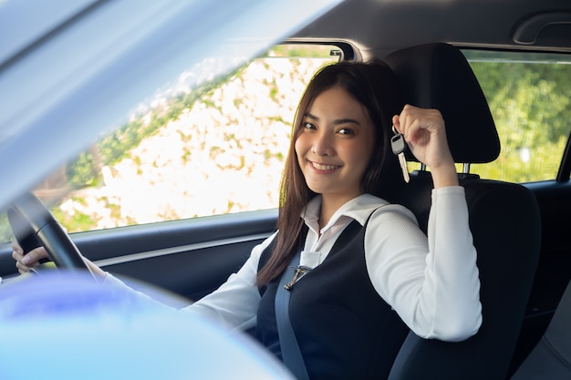 Asian woman driver smiling and showing new car keys and sitting inside the car