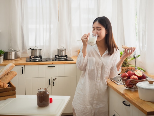 부엌에서 빵과 음료 우유를 먹는 아시아 여자