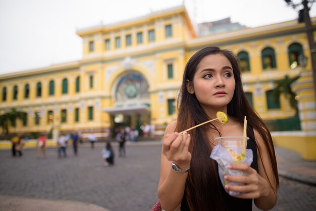 Asian woman eating in front of Saigon Central Post Office