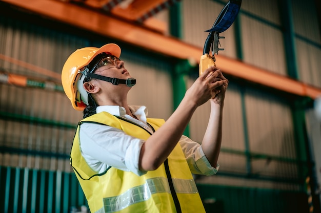 Asian woman engineer uses remote control panel to lift up or down of power trolley crane