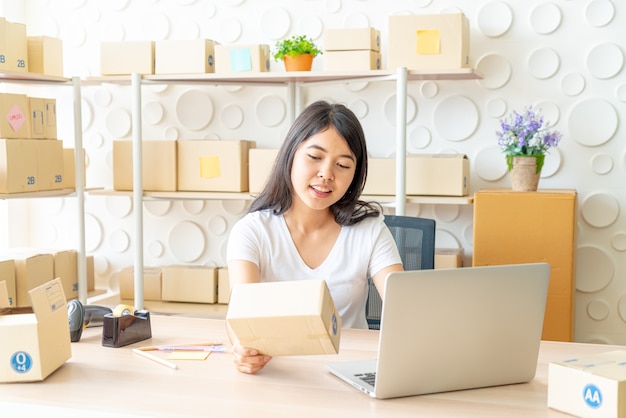 Asian woman enjoy herself while using internet on laptop and phone in office - sell online or online shopping concept