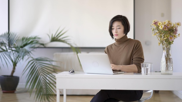 흰색 홈 오피스에서 노트북으로 작업하는 안경을 쓴 아시아 여성