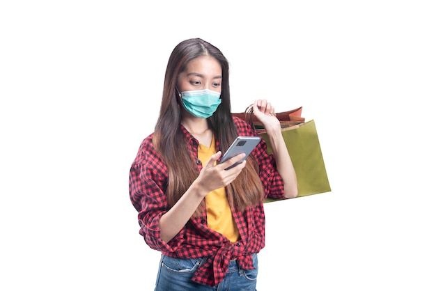 Asian woman in face mask holding mobile phone while carrying shopping bags isolated over white background