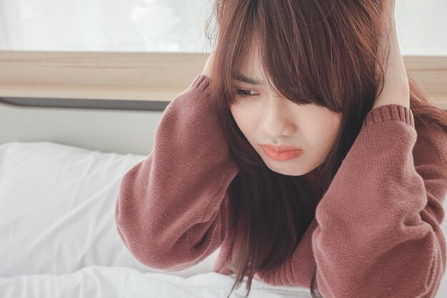 Asian woman feel headaches and discomfort on bed in white bedroom morning