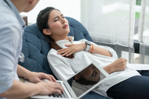 Asian woman feeling chest pain lying on the sofa while doctor asking her symptoms