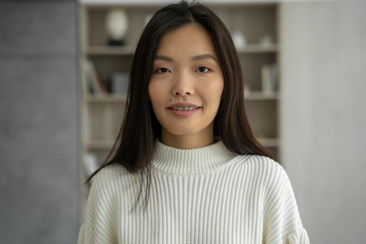 Photo 아시아 여성은 행복한 미소를 느끼고 거실에 서 있는 카메라를 본다