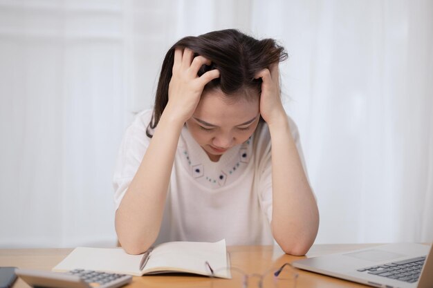 Asian woman feels upset and uncomfortable during working with a\
lot of document and overworking stressful and upset asian young\
businesswoman catching at her head woman worried about working\
problem