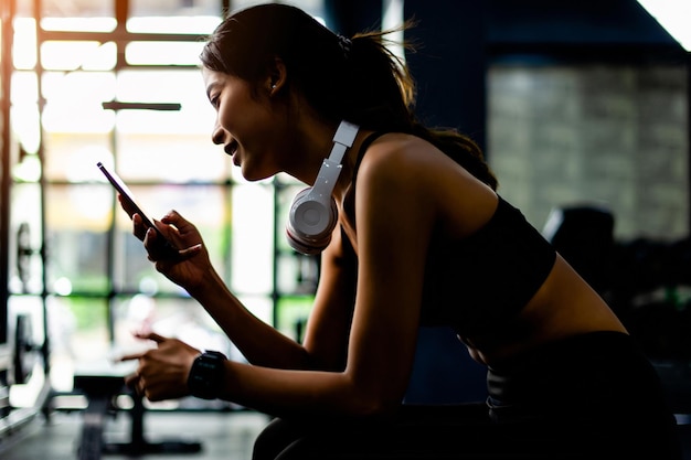 Foto la donna asiatica in abiti da fitness seduta sul telefono bianco e le cuffie si rilassano durante l'esercizio creano energia per l'ispirazione del fitness