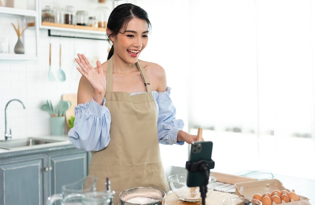 Asian woman food blogger cooking cake in front of smartphone camera while recording vlog video