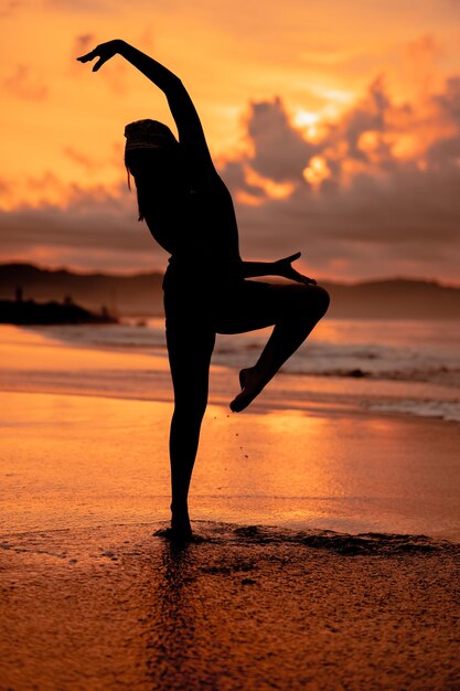 An Asian woman in the form of a silhouette doing ballet movements very agile on the beach