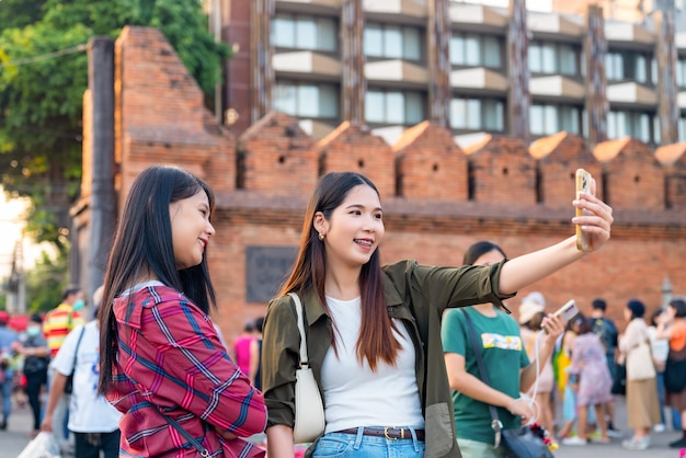 Asian woman friends using smartphone taking selfie or vlogging during travel together in Chiang Mai city Thailand Attractive girl enjoy outdoor lifestyle travel city street on summer vacation