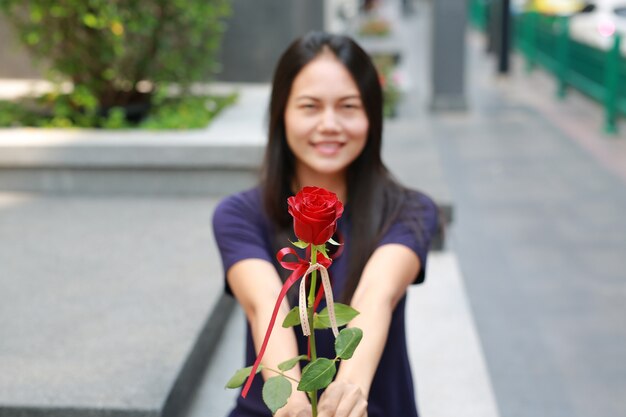 Asian woman giving the rose for you. Focus at the flower.