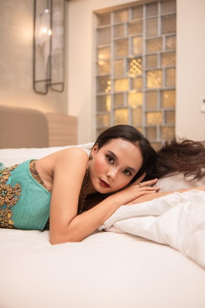 an Asian woman in a green dress is sleeping on a white bed in a luxury hotel at night