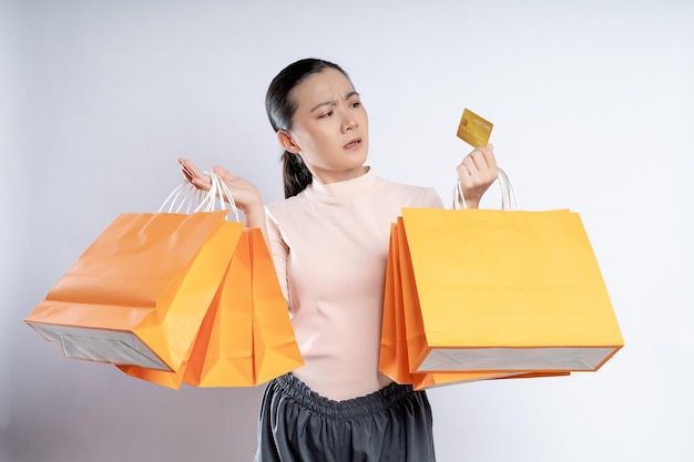 Фото Азиатская женщина виновата, нервничая, держа в руках больше сумок и кредитных карт, изолированных на заднем плане