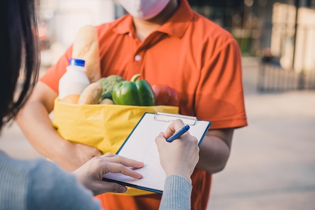 写真 プロの配達員からの食品果物野菜配達のバッグを受け入れるアジアの女性の手