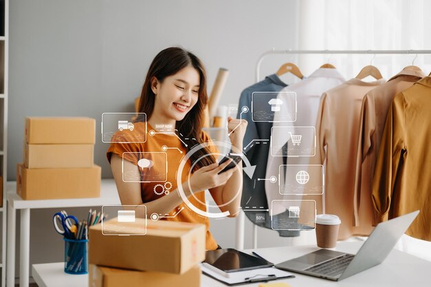 Asian woman hand using a laptop smartphone and tablet and writing notebook at the office of her business online shopping in home with virtual icon