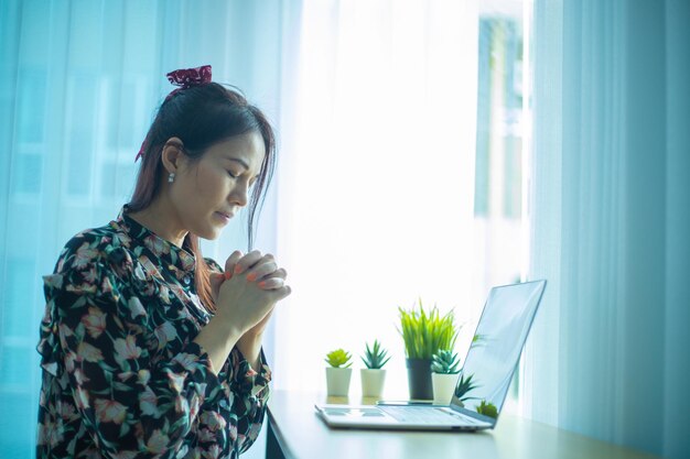 Asian woman hands praying with laptop at home Church services online concept