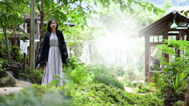 Asian woman happily walking and taking pictures in nature park, she looks at camera and smiles.