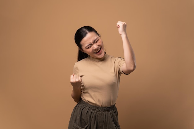 Asian woman happy confident standing showing her fist make a winning gesture isolated on beige background