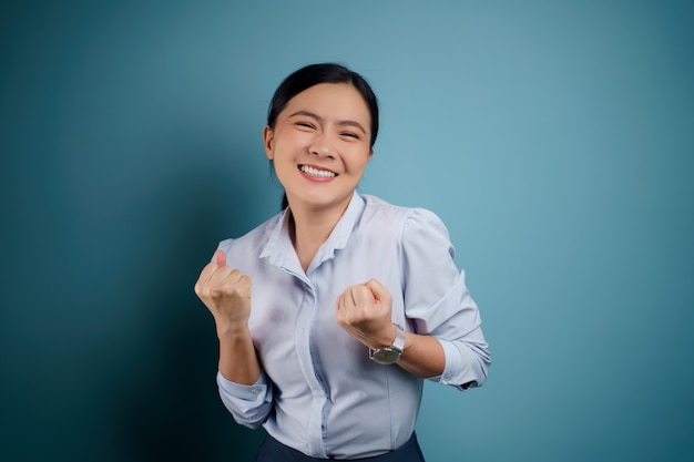 Asian woman happy confident standing showing her fist make a winning gesture isolated on blue.