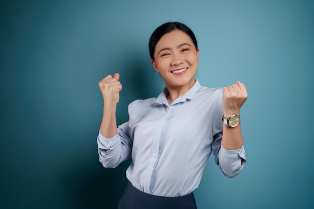 Asian woman happy confident standing showing her fist make a winning gesture isolated on blue.