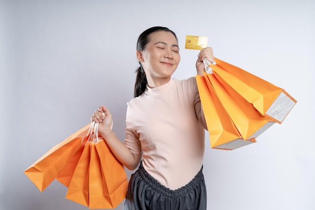 흰색 배경에 격리된 쇼핑백과 신용카드를 들고 행복한 미소를 짓고 있는 아시아 여성