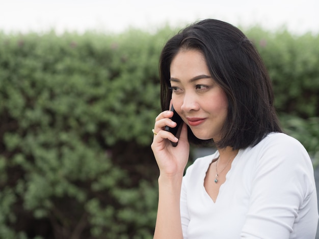 Азиатская женщина имеет хороший счастливый разговор по мобильному телефону.