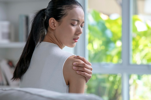 Asian woman has shoulder pain Female holding painful shoulder with another hand People with bodymuscles problem Healthcare And Medicine