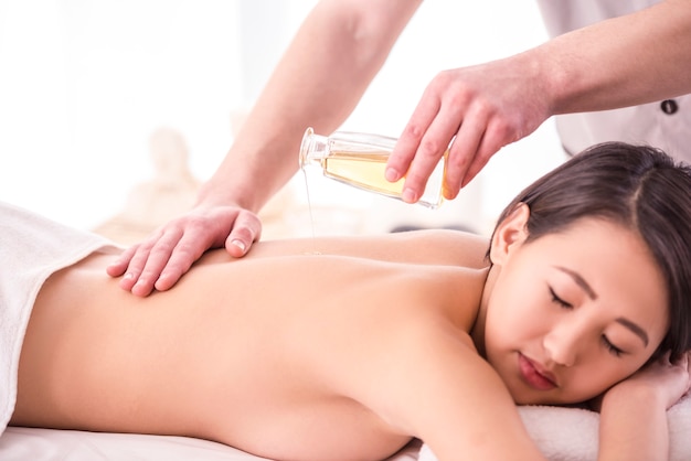 Asian woman having massage with spa oil in beauty salon.