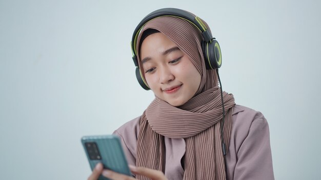 Asian woman in hijab looking at phone screen while listening at home