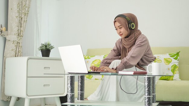 Asian woman in hijab working from home typing laptop while listening