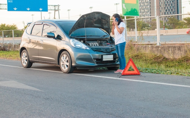 Азиатская женщина, держащая мобильный телефон ходьба вокруг автомобиля. машина сломалась