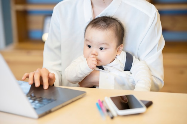아시아 여자 아기를 안고 실내에서 노트북을 운영