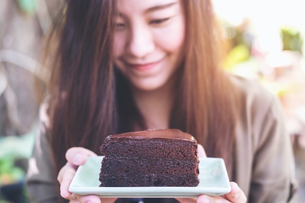 現代のカフェで幸せと良いライフスタイルを感じるとブラウニーケーキを保持しているアジアの女性