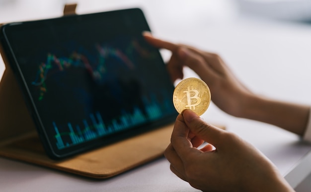 Photo asian woman holding coin in hand while watching stock chart