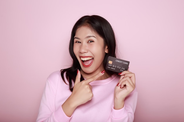 Photo asian woman holding a credit card in her hand holding a debit card in hand a beautiful young woman was feeling very happy and excited portrait on a light pink background