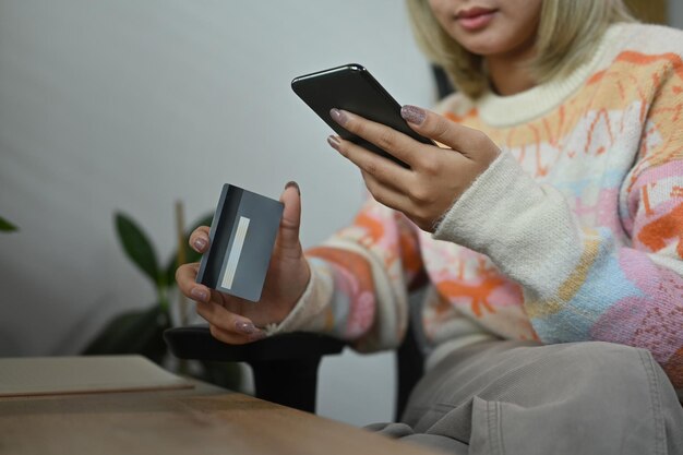 Asian woman holding credit card and shopping online with smart phone at home