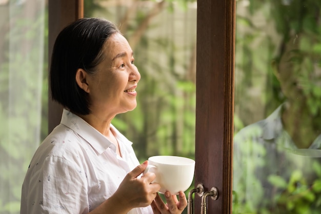 asian woman holding a cup of tea and looking outside