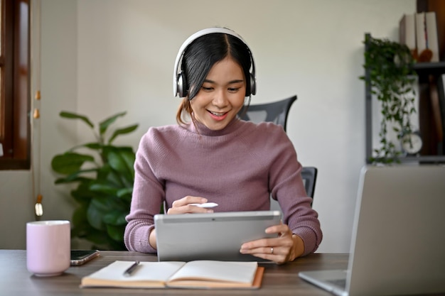 An Asian woman holding digital tablet while woking at her home office sitting at her desk