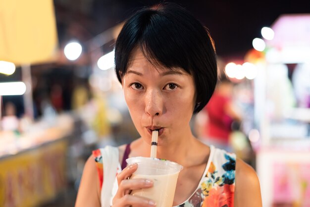 Donna asiatica che tiene il famoso tè al latte a bolle taiwanese al mercato notturno