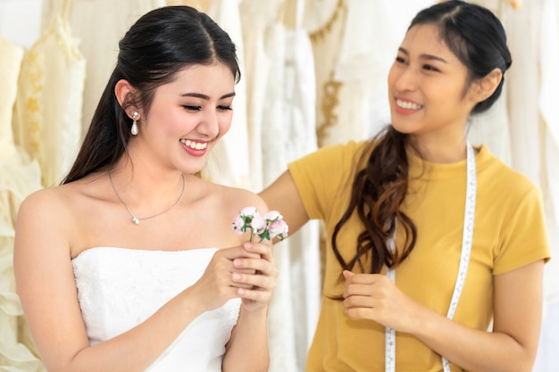 Asian woman holding flower measuring on wedding dress in a shop by the tailor.