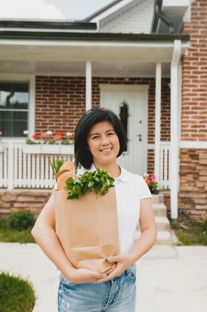 Asian woman holding a grocery bag with vegetables near her house