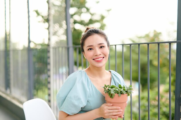 Asian woman holding and looking at plant potted on balcony at apartment in the morning