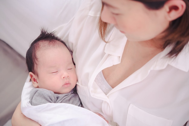 Asian woman holding a newborn baby in her arms at home.