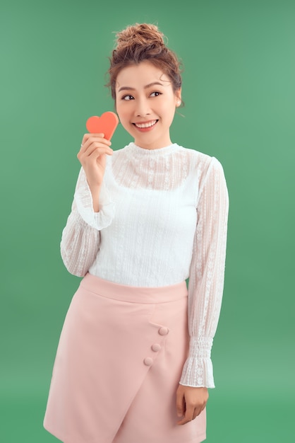 Photo asian woman holding paper heart shaped card over green background. valentine day concept.