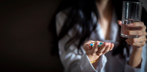 Asian woman holding pills and a glass of water