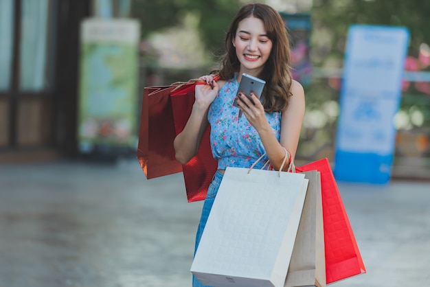 Sacchetti della spesa e smartphone asiatici della tenuta della donna in mani