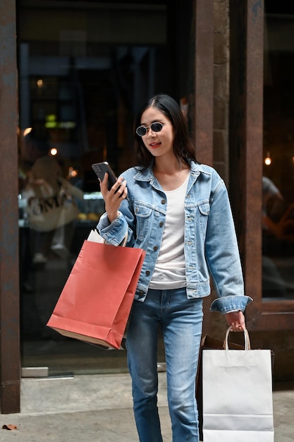 Asian woman holding smartphone and carrying shopping bags while
enjoys shopping at city mall