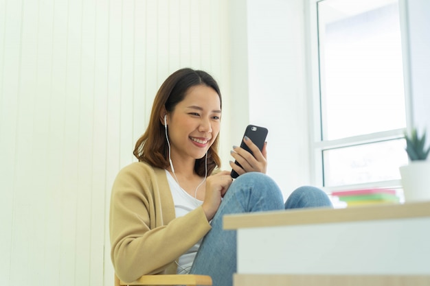 Asian woman holding smartphone to communicate with friends and family inside houses's living room