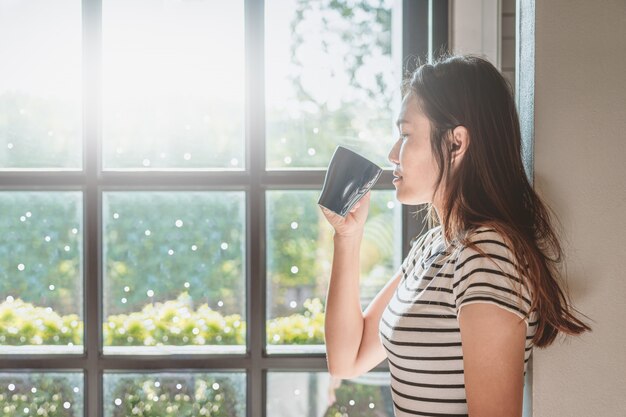 アジアの女性は彼女の家でホットコーヒーを飲んでいます。